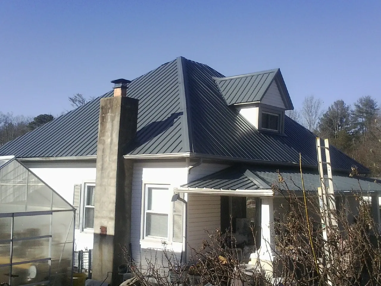 Dark blue standing seam metal roof on a white farmhouse with dormer — Slate & Tile Roof Repair by Roofing Brothers in Whitestone
