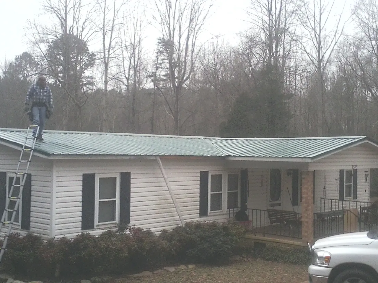 Worker on a ladder beside a new green metal roof on a ranch home in Whitestone