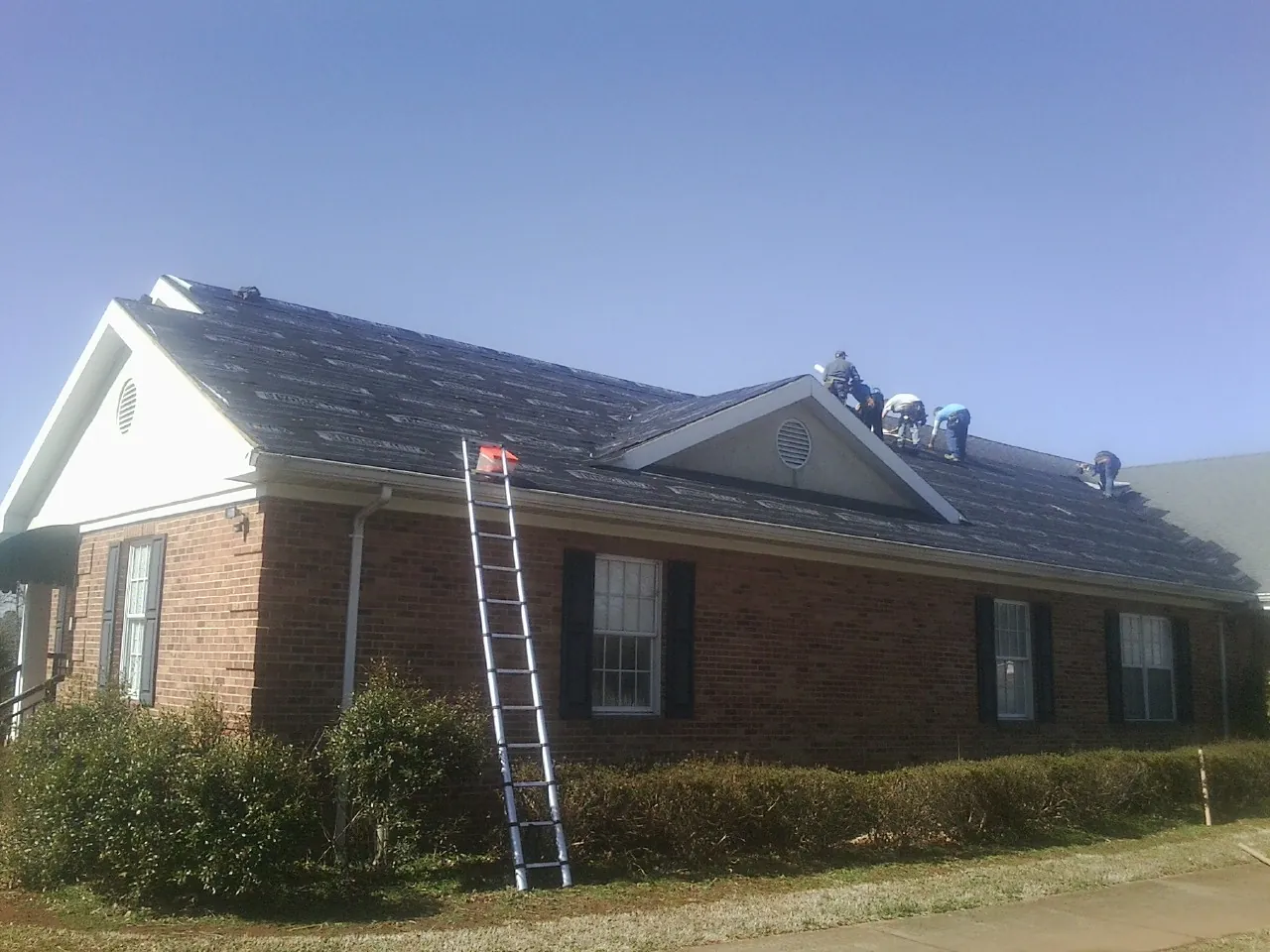 Crew tearing shingles off a brick ranch roof with a ladder set — Metal Roof Repair work by our crew in Whitestone