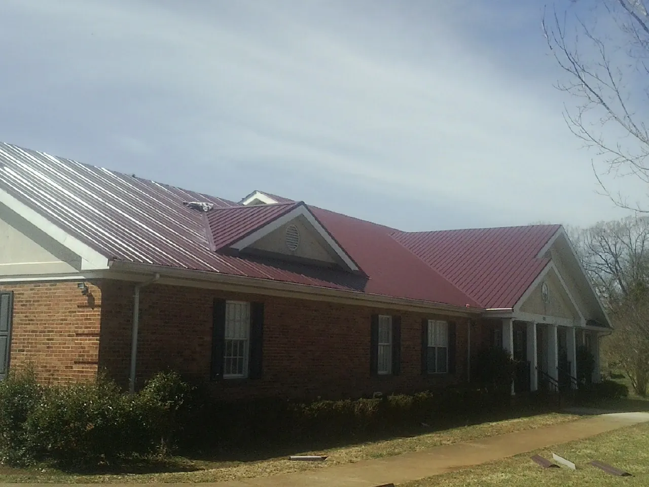 Red metal roof with gabled entries on a long brick building, from a Hail Damage Roof Repair job in Whitestone
