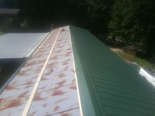 Old rusted panels beside newly installed green metal roofing — Wind Damage Roof Repair by Roofing Brothers in Whitestone
