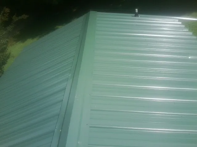 New green metal panels meeting at the ridge of a roof — Flat Roof Repair work by our crew in Whitestone
