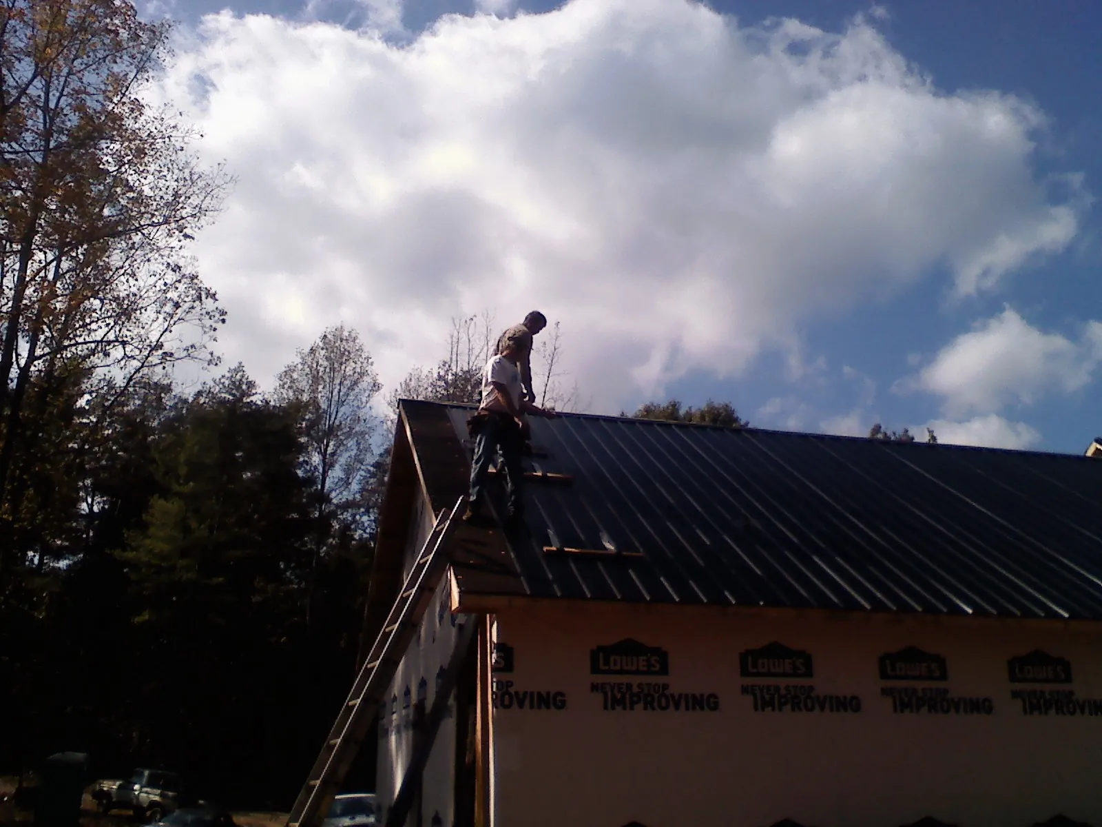 Roofer fastening dark metal panels high against a cloudy sky, from a Roof Inspection job in Whitestone